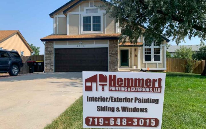 Hemmert Painting & Exteriors signage with a contact number and a house painting project