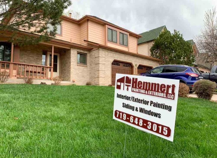 Hemmert Painting & Exteriors signage with a contact number and a house painting project