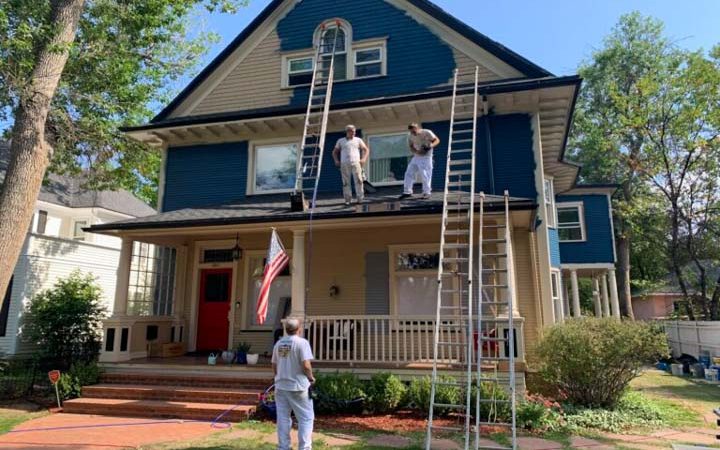 two painters standing on the porch roof of a three-story house checking their remaining paint on hand. painting the sidings of the house
